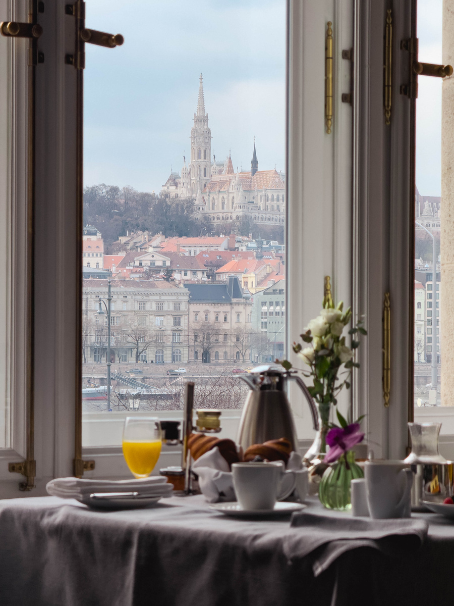 Breakfast is set before an open hotel window framing Matthias Church and the Buda skyline across the Danube.
