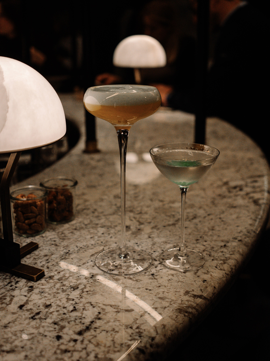 Two sculptural cocktails stand among small table lamps in the evening light of MÚZSA.