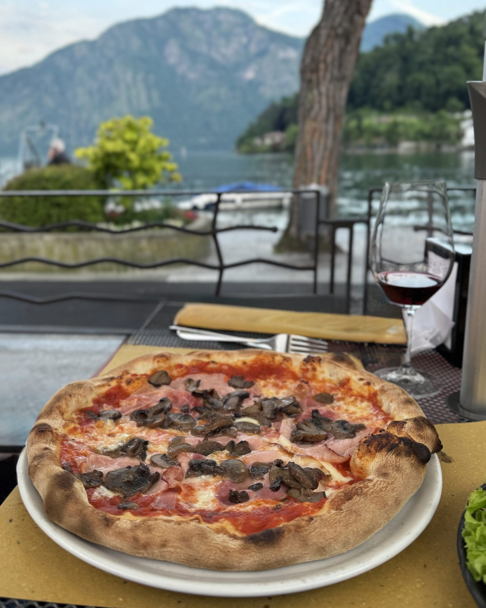 A mushroom and ham pizza with a glass of red wine at a lakeside table in Lenno.