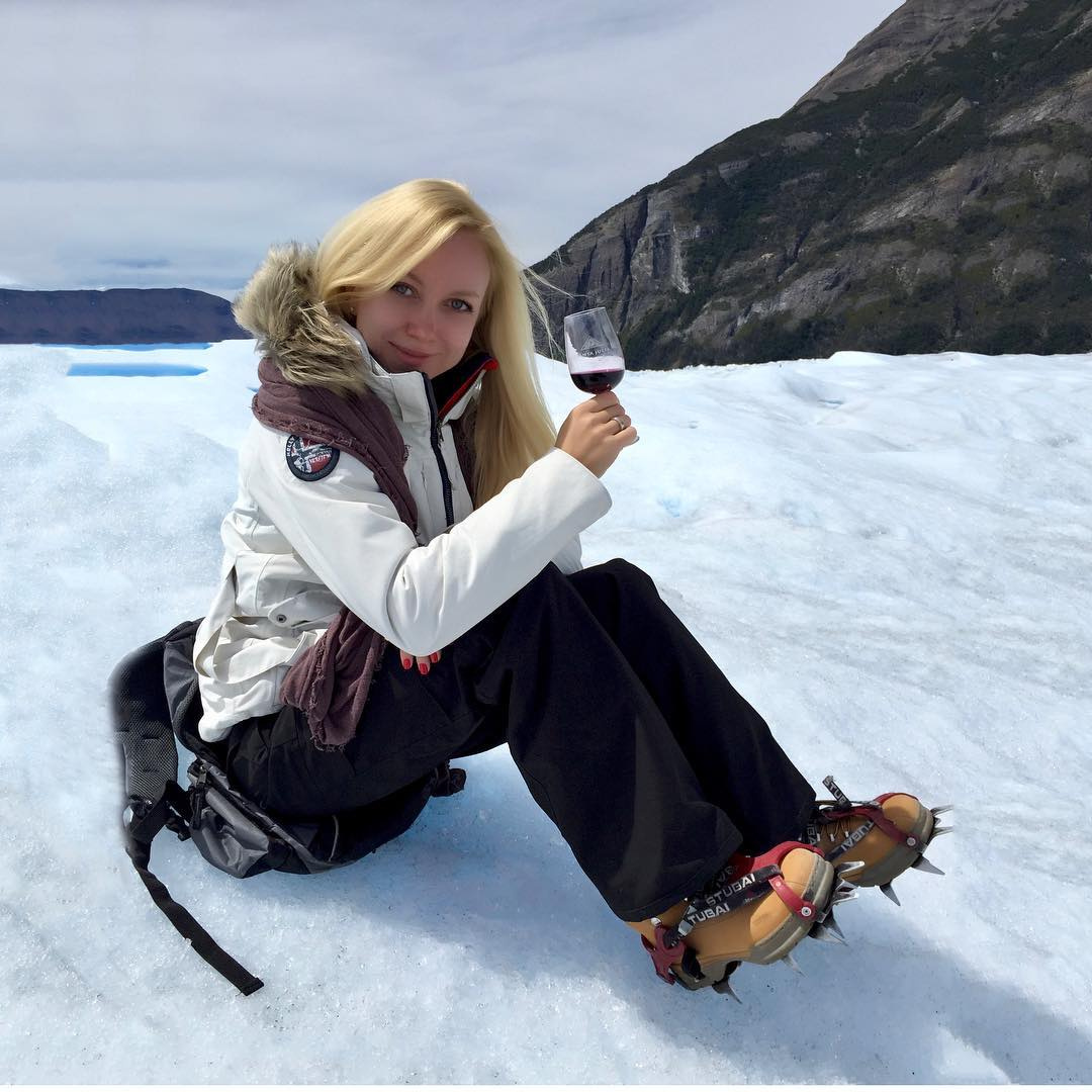Olga seated on the Perito Moreno Glacier holding a glass of red wine.