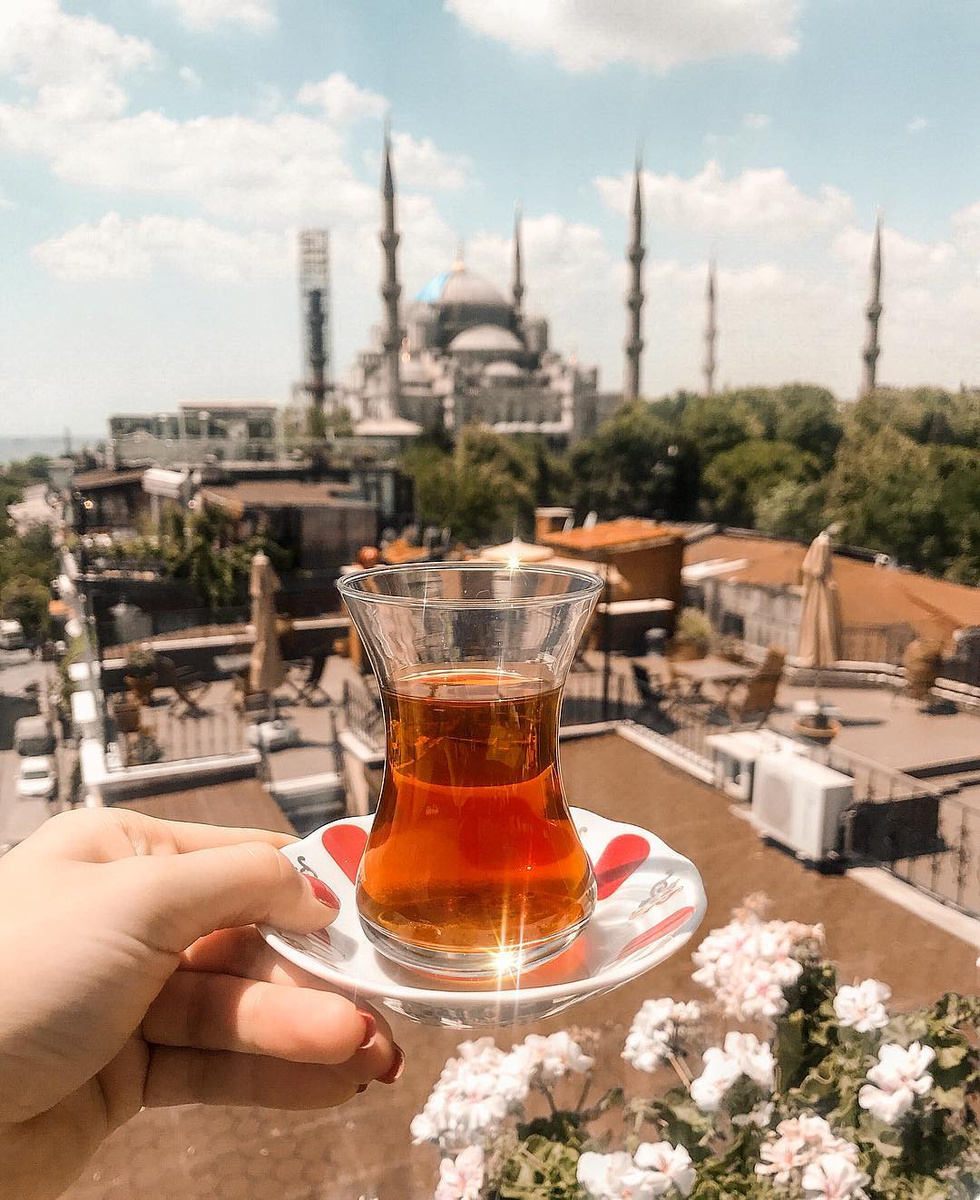 A glass of Turkish tea held above Istanbul rooftops with the Blue Mosque beyond.