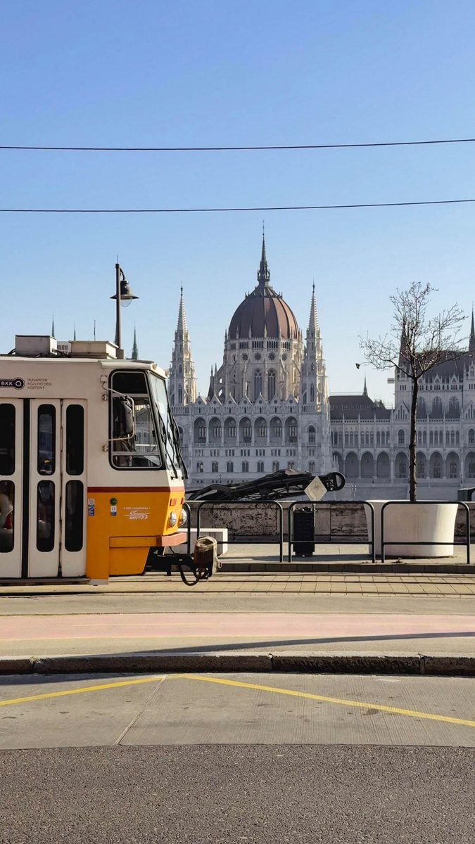 A yellow Budapest tram passes the Hungarian Parliament Building on a clear winter morning.