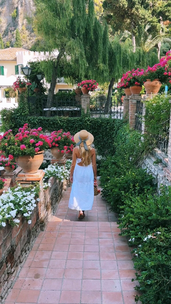 Olga walking through a flower-filled garden above the sea in Taormina.