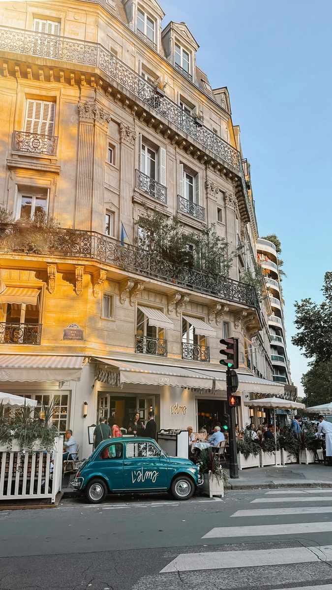 A sunlit Paris street lined with cream Haussmann façades and café tables.