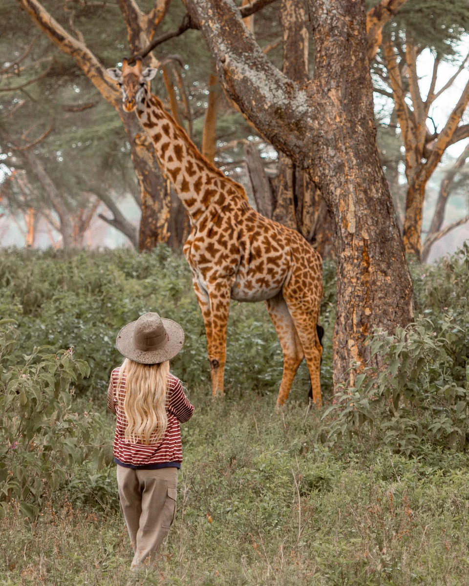 Olga standing close to a giraffe among trees in Kenya.