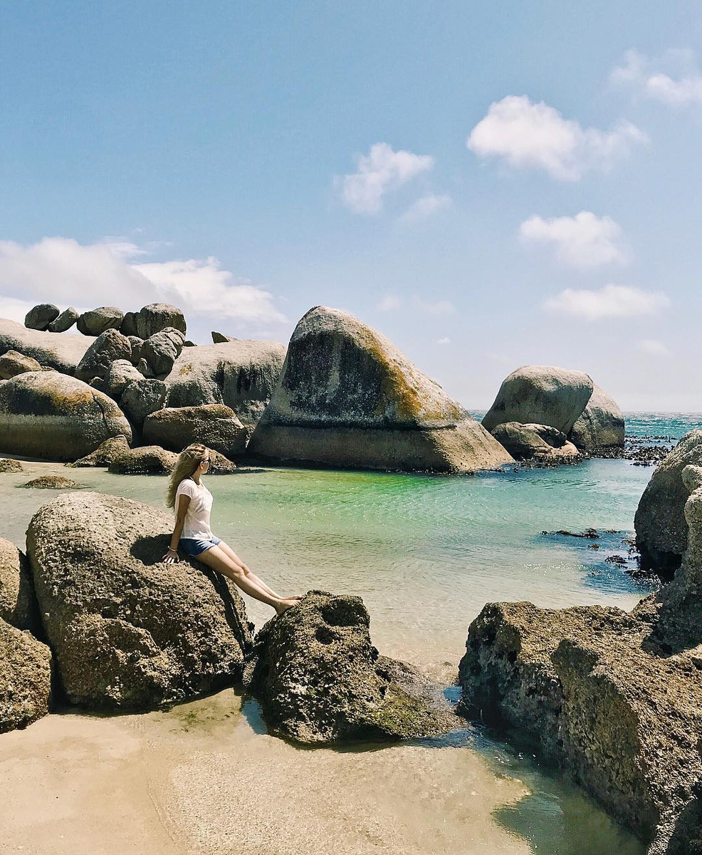 Olga seated among granite boulders beside the clear water at Boulders Beach.