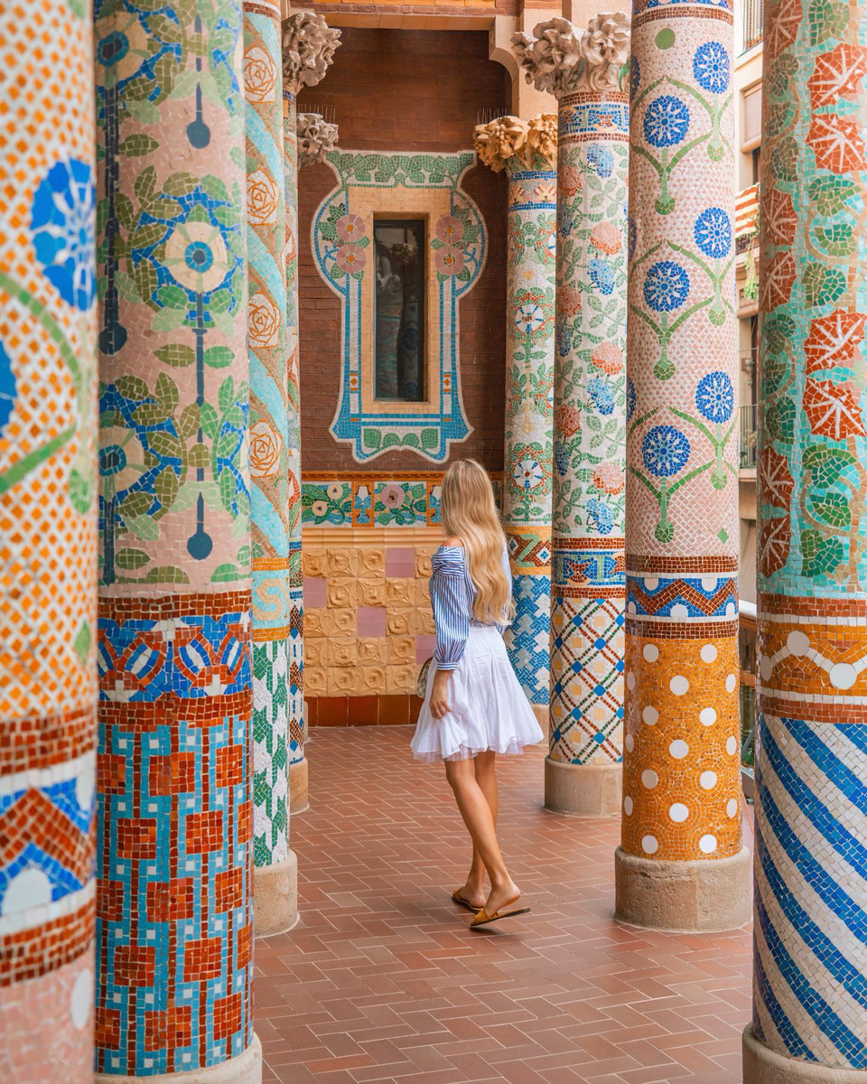 Olga walking between brightly tiled columns in Barcelona.