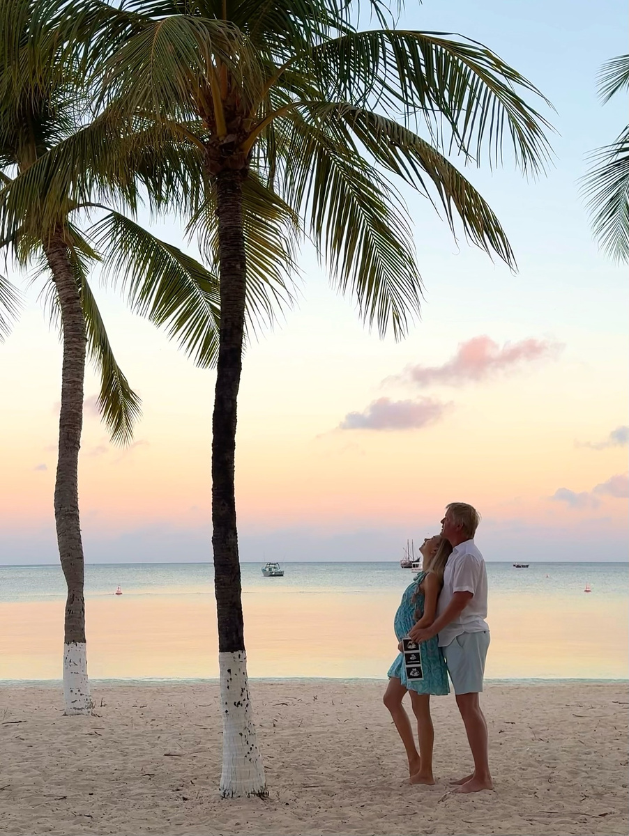 A couple beneath palm trees beside the sea at sunset in Aruba.