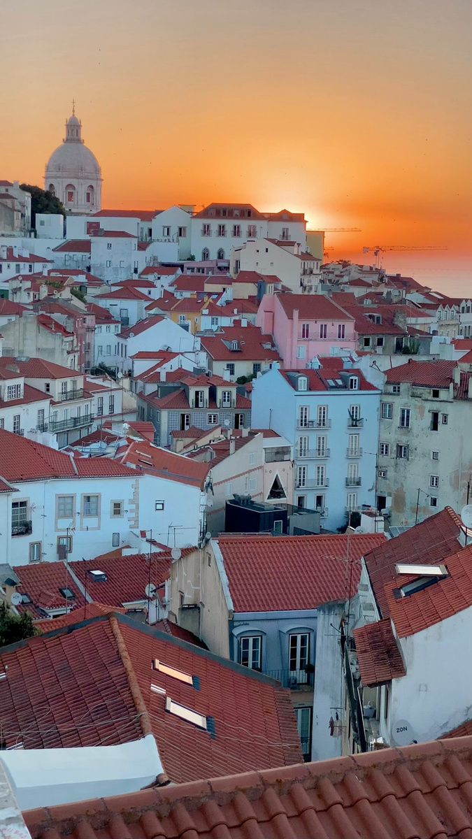 Lisbon’s red rooftops and hills beneath a glowing sunset.
