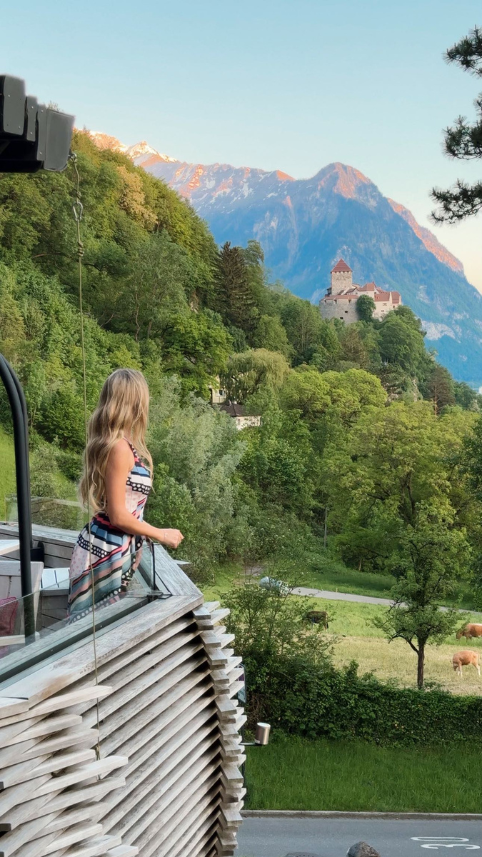 Olga looking across green slopes towards Vaduz Castle in Liechtenstein.