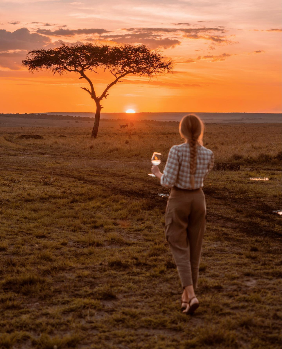 Olga watching an orange sunset beside an acacia tree on the Kenyan savannah.