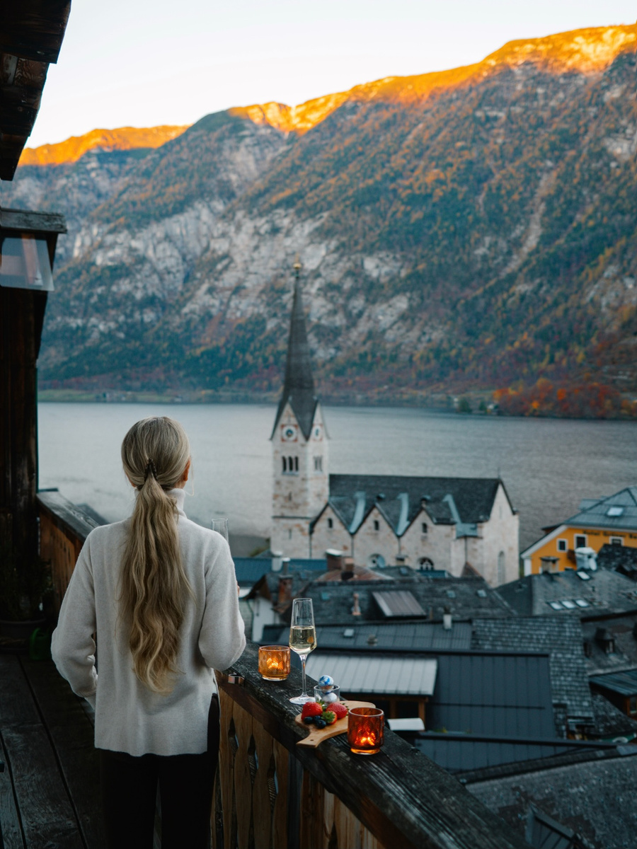 Olga on a balcony above Hallstatt as evening light reaches the mountains.