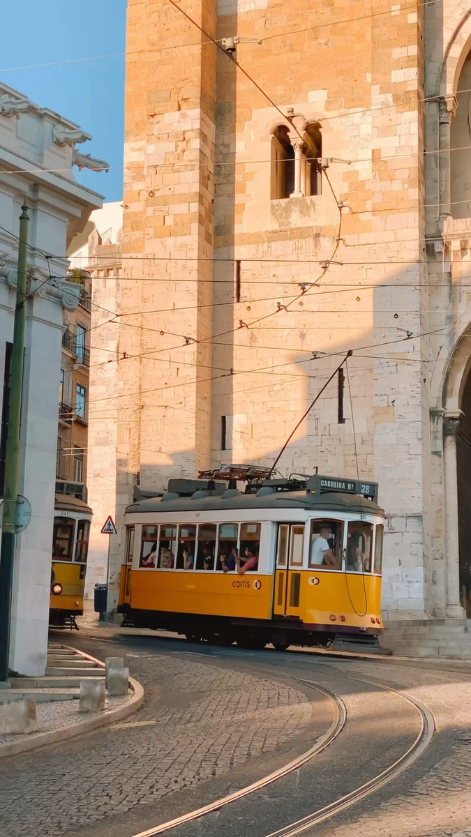 A yellow Lisbon tram passing an ornate stone building.