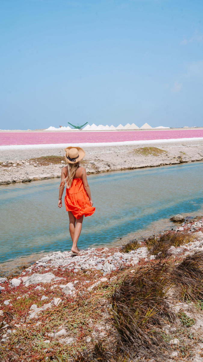Olga in an orange dress beside Bonaire’s pink salt flats.