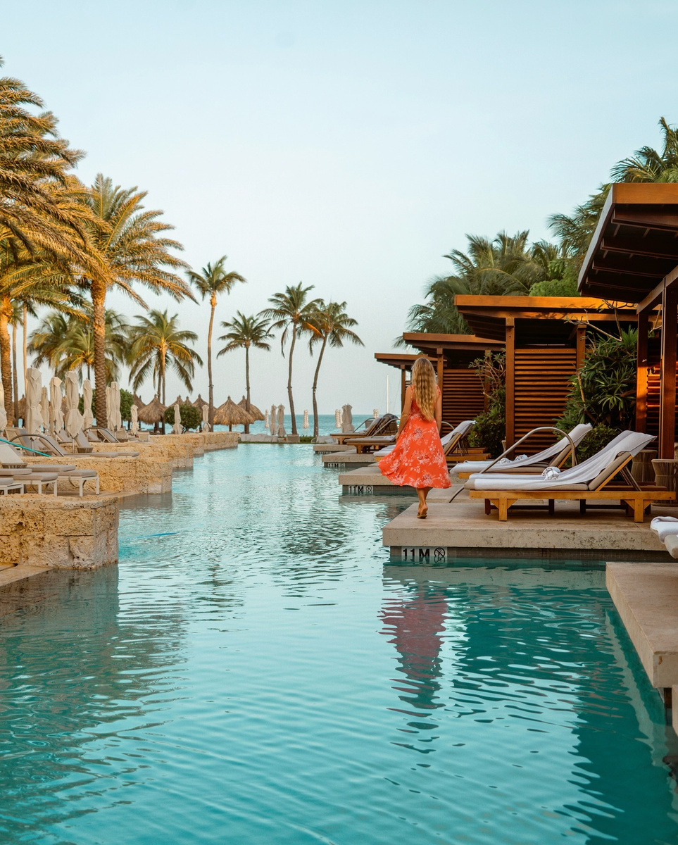A palm-lined resort pool beneath a bright blue sky in Aruba.