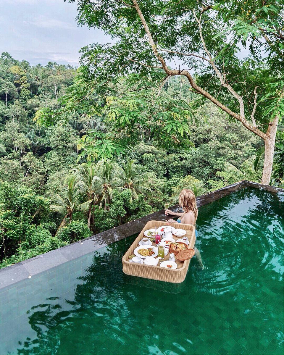 Olga beside a floating breakfast tray in a pool surrounded by Ubud forest.