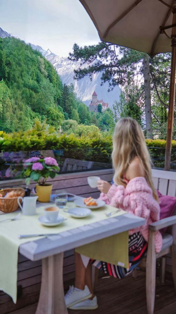 Olga at breakfast on a garden terrace overlooking Alpine slopes in Liechtenstein.