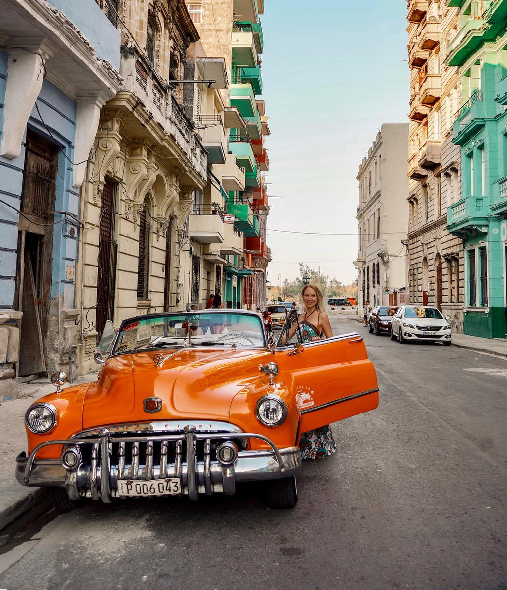 Olga beside an orange vintage convertible on a street in Havana.