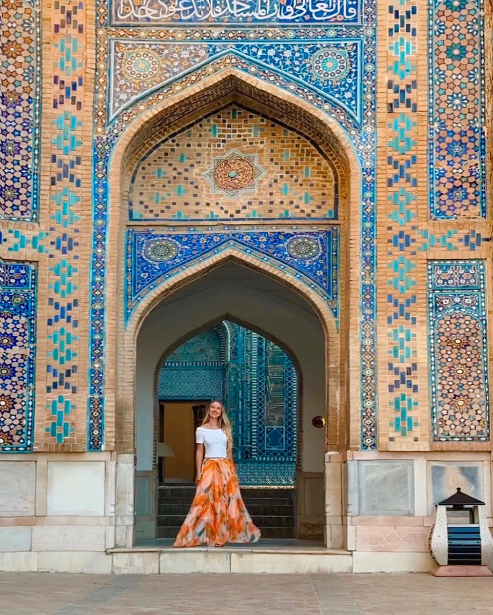 Olga in an orange dress before a blue-tiled portal in Samarkand.