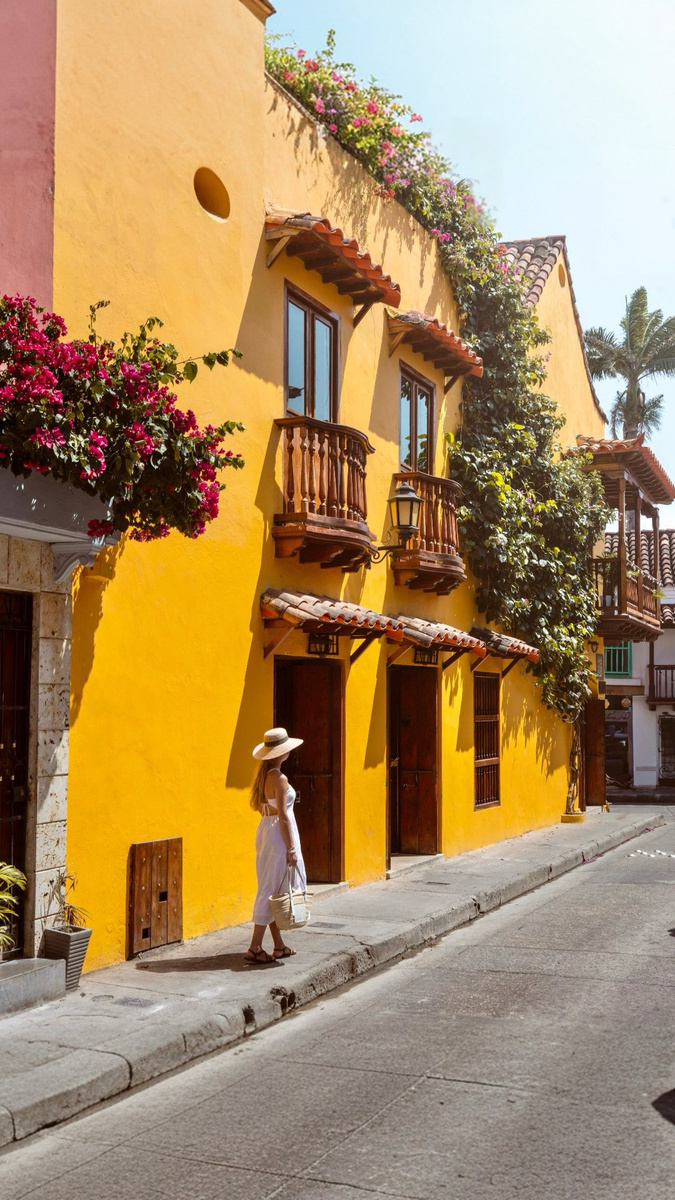 Olga walking along a yellow colonial street with flowering balconies in Cartagena.