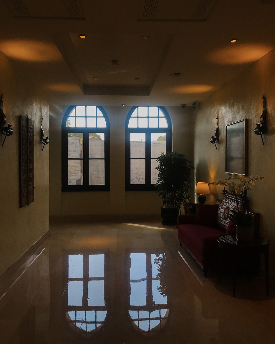A softly lit corridor at Four Seasons Sultanahmet with arched windows reflected in a polished floor and a red chair.