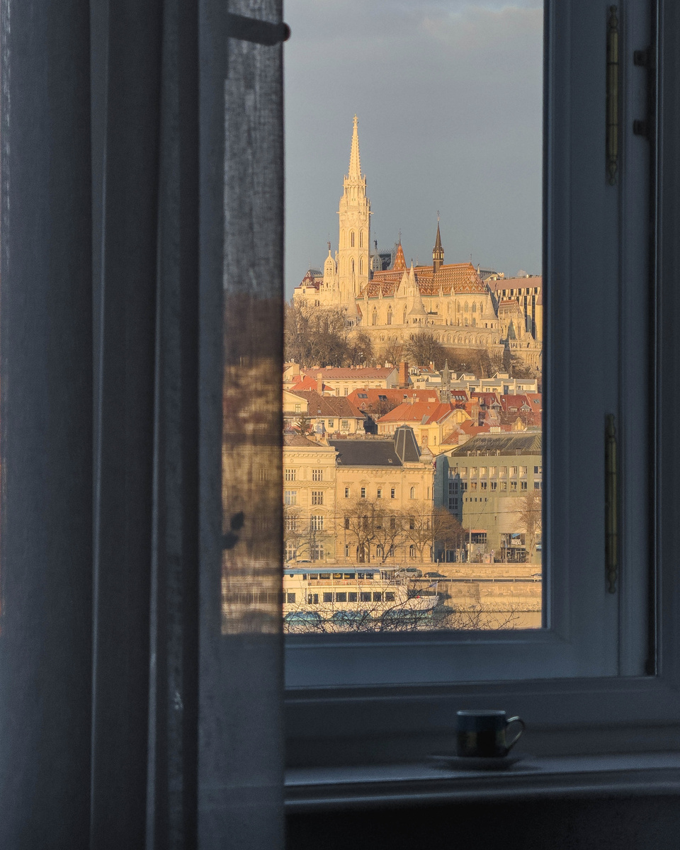 Matthias Church and the Buda skyline appear through a dark-framed guest-room window.