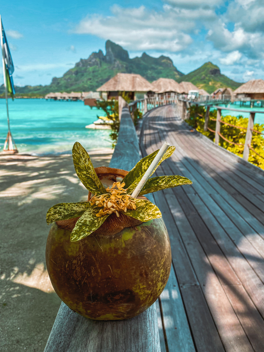 Fresh coconut resting on a wooden boardwalk with overwater bungalows and Mount Otemanu beyond