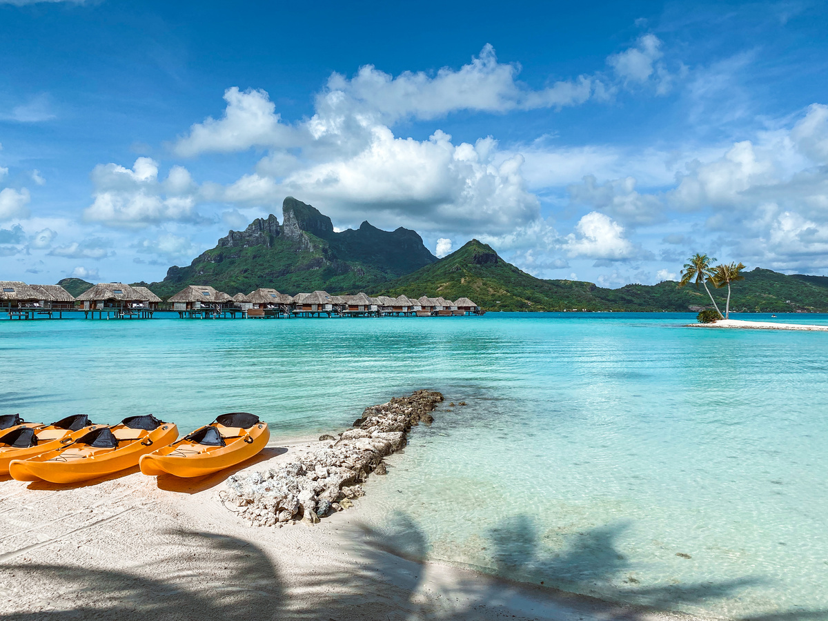 Red and yellow kayaks on the beach beside the clear blue lagoon at Four Seasons Bora Bora