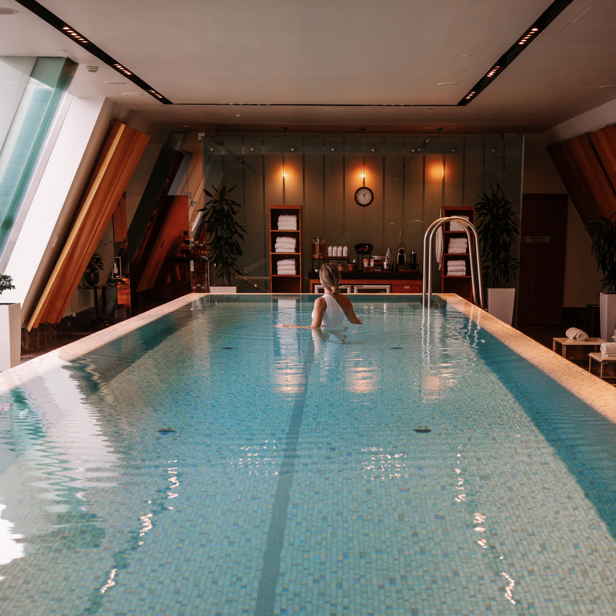 The rectangular indoor pool stretches beneath sloping glass windows and warm wall lights.