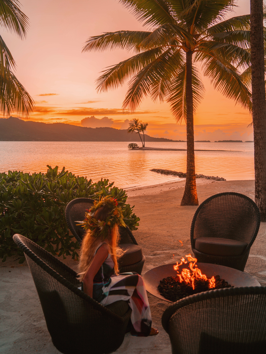 Olga beside a fire pit at sunrise with the Bora Bora lagoon and Mount Otemanu beyond