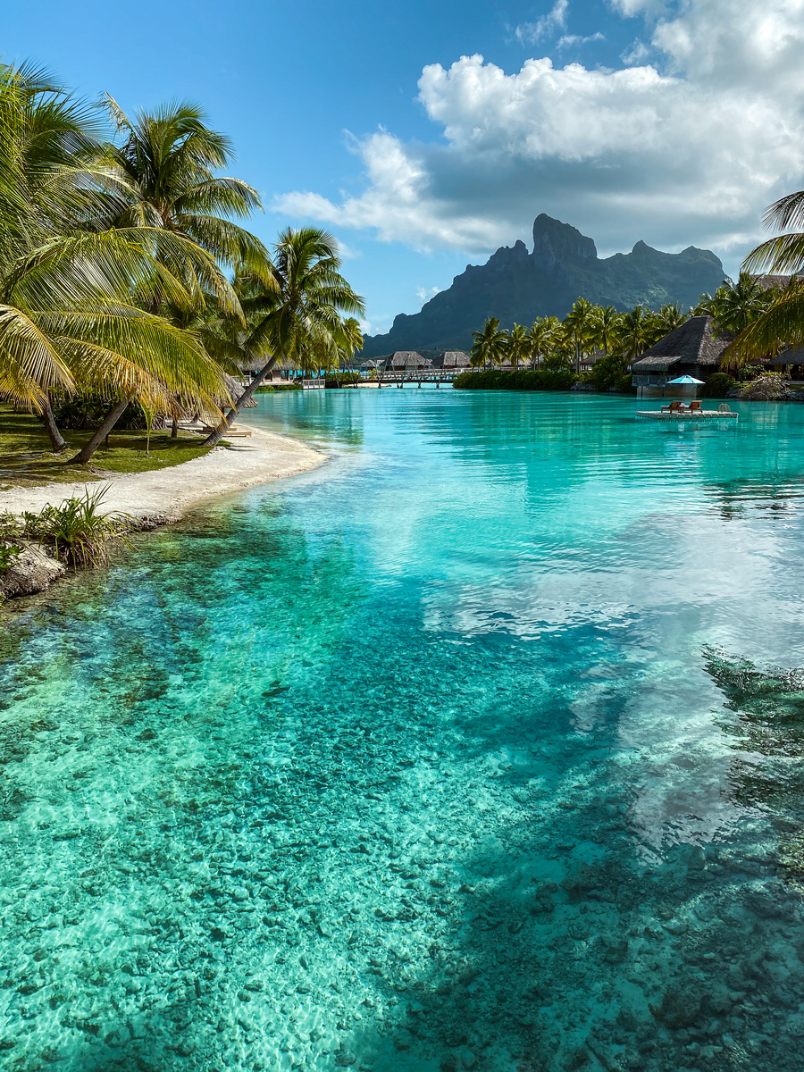 Clear turquoise lagoon channel winding between palms and bungalows at Four Seasons Bora Bora