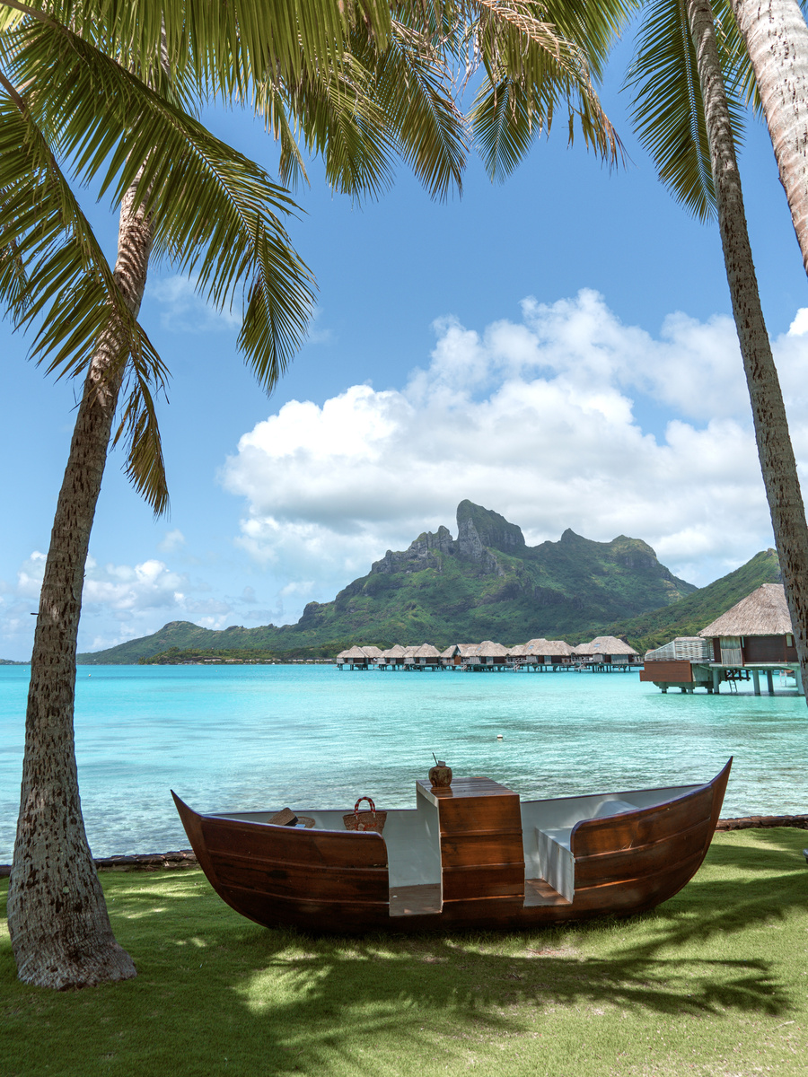 Carved wooden canoe displayed on grass beneath palm trees at Four Seasons Bora Bora