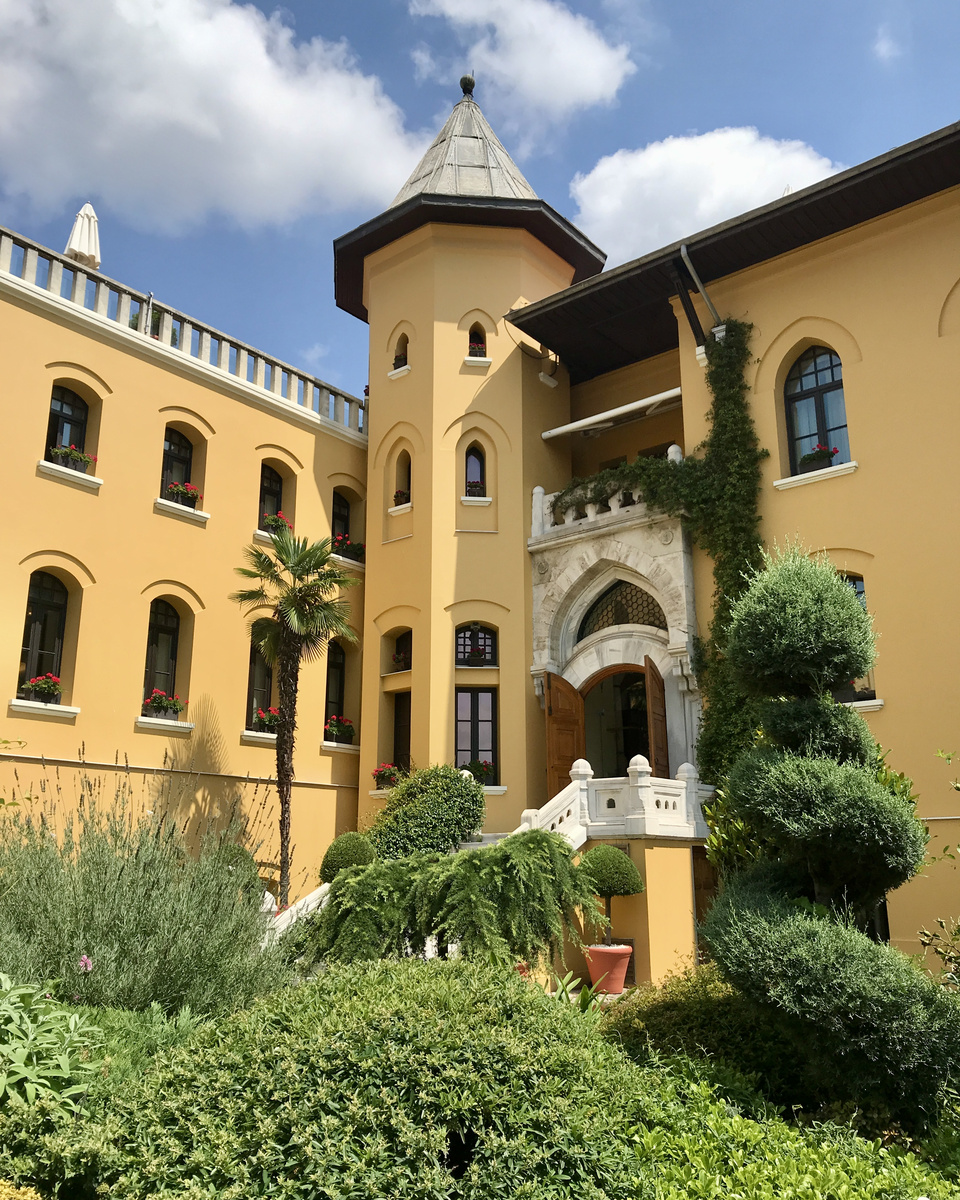 The ochre exterior, arched windows, corner tower and marble entrance of Four Seasons Sultanahmet rise above the garden.
