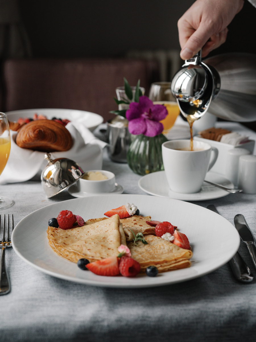 Coffee is poured beside French toast, berries, juice and flowers on the in-room breakfast table.