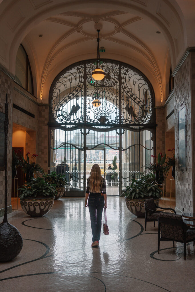 Olga walks towards the ornate glass entrance doors beneath the vaulted lobby of Four Seasons Gresham Palace.