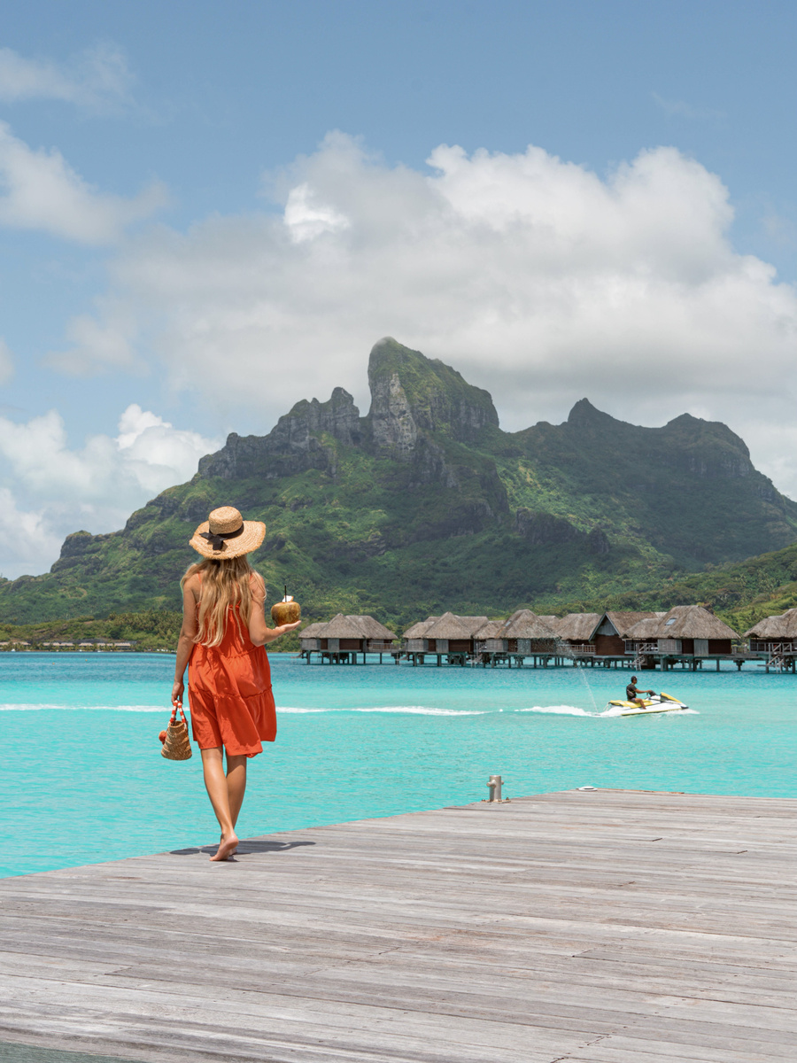 Olga sitting at the end of a wooden pier above the clear lagoon at Four Seasons Bora Bora