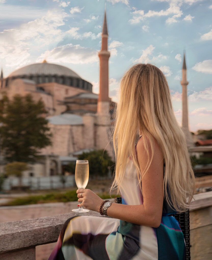 Olga sits with a glass of sparkling wine on the Four Seasons Sultanahmet roof terrace, with Hagia Sophia behind her at sunset.