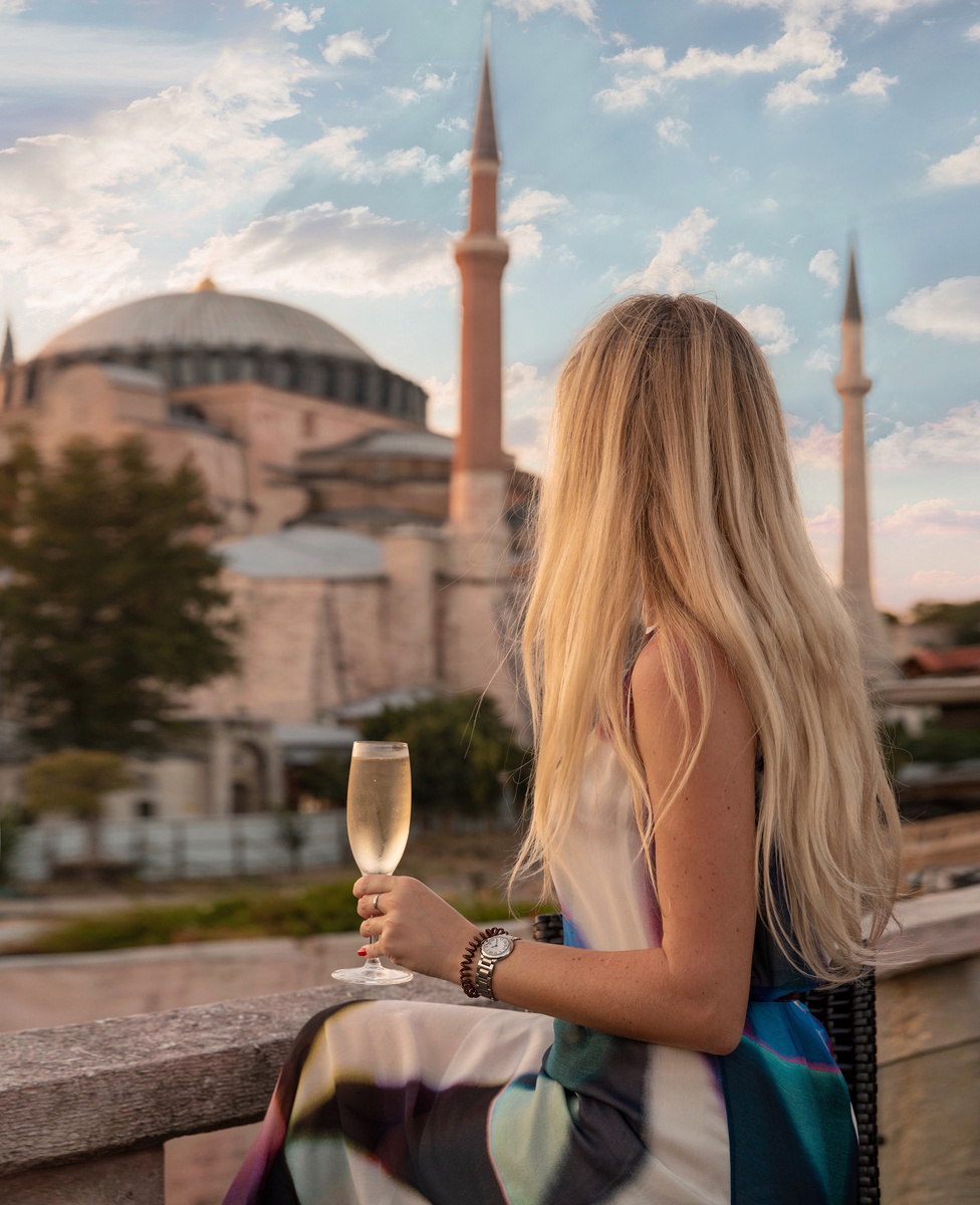 Olga sits with a glass of sparkling wine on the Four Seasons Sultanahmet roof terrace, with Hagia Sophia behind her at sunset.