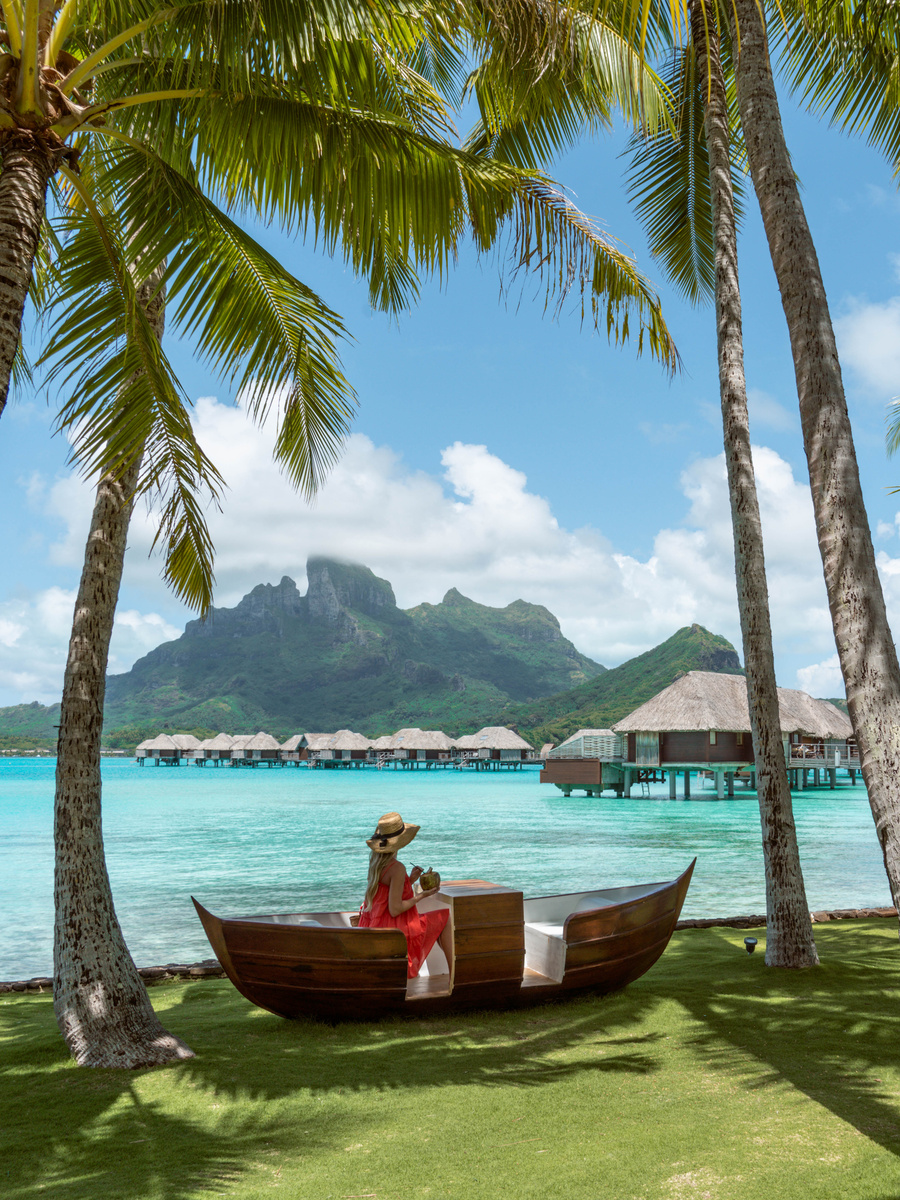 Olga sitting in a carved wooden canoe on a lawn beneath palm trees at Four Seasons Bora Bora