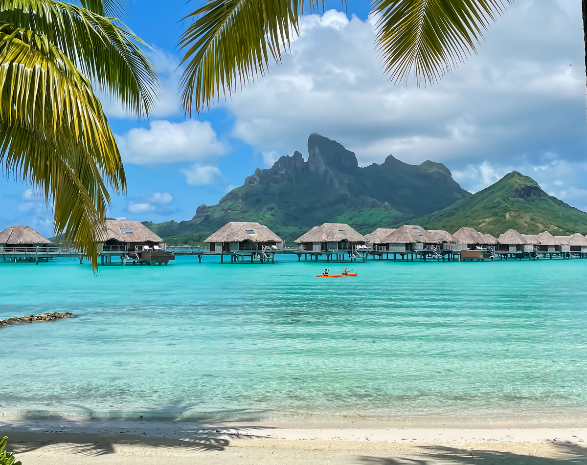 Wide white-sand beach beside a luminous blue lagoon and overwater bungalows at Four Seasons Bora Bora