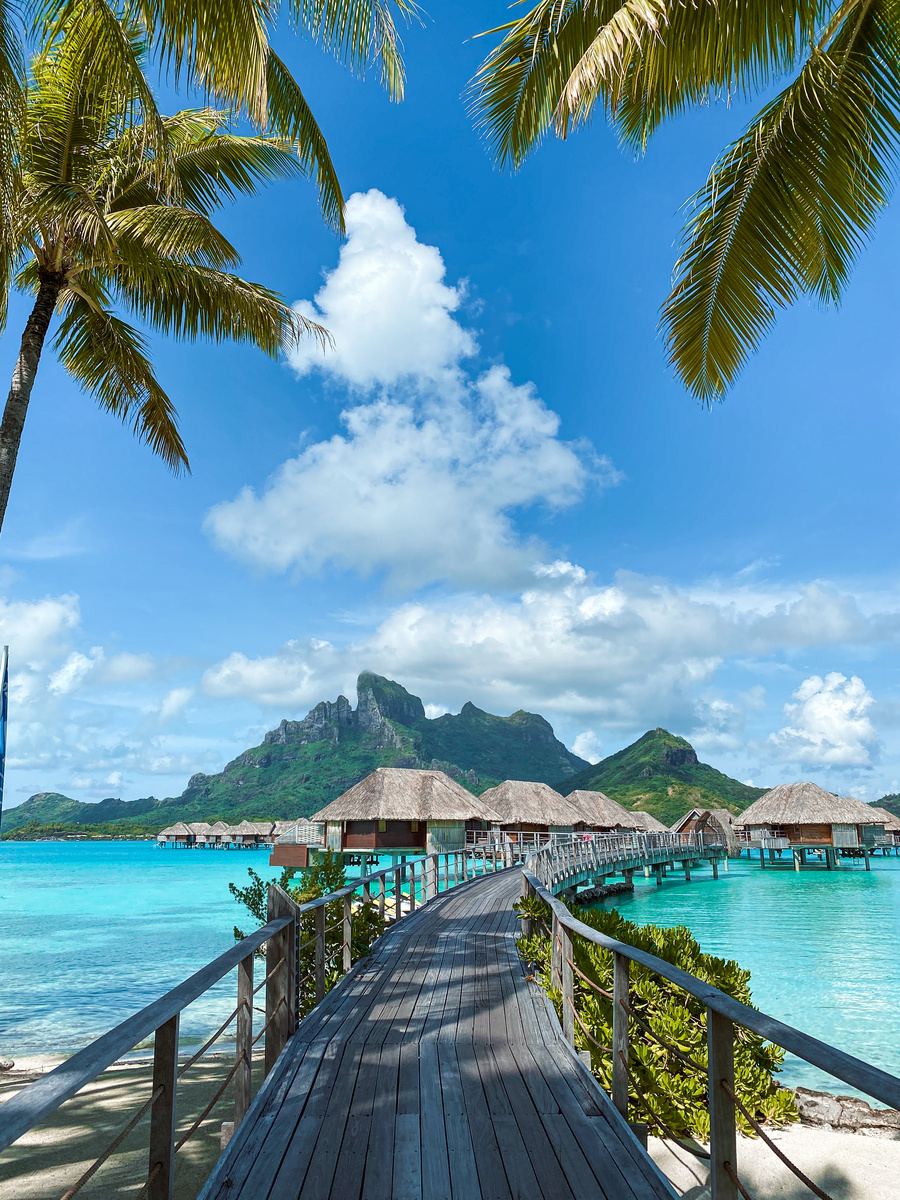 Wooden boardwalk curving between overwater bungalows above the turquoise lagoon at Four Seasons Bora Bora
