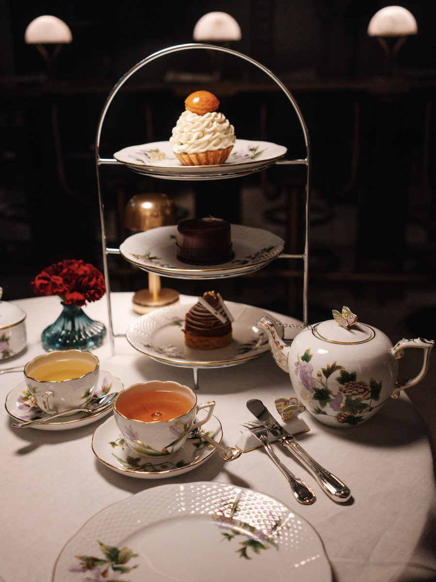 A tiered stand of pastries and sandwiches rises above tea served on floral china at MÚZSA.