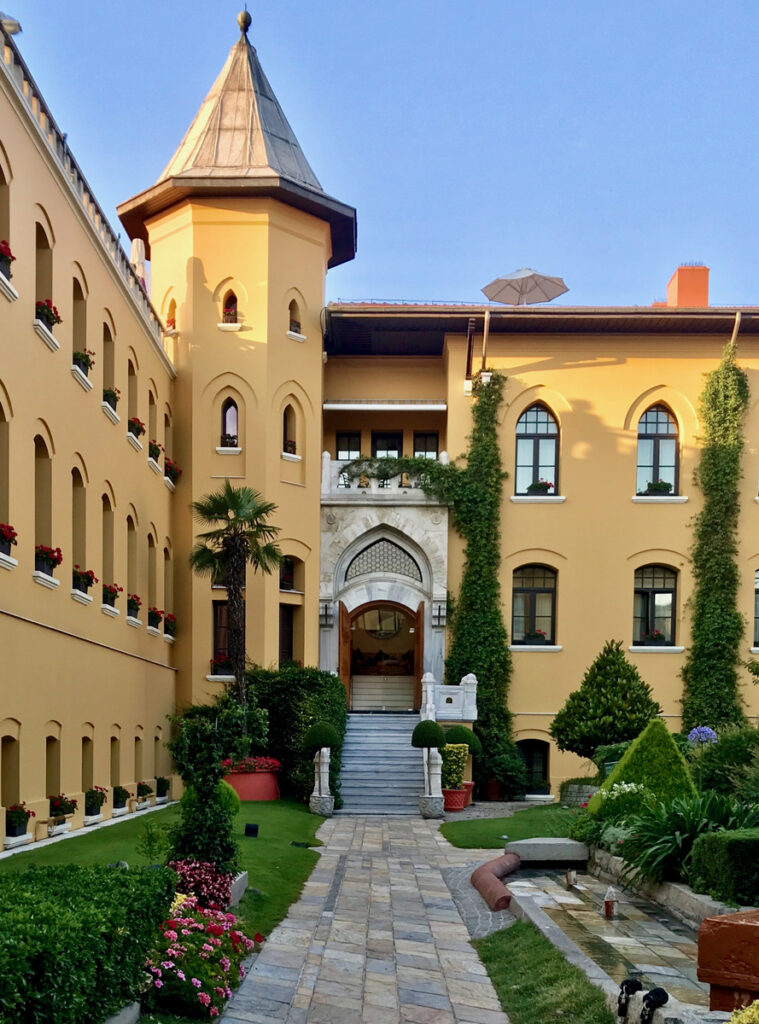 Four Seasons Sultanahmet’s ochre courtyard facade, pointed arched entrance, corner tower and garden path.