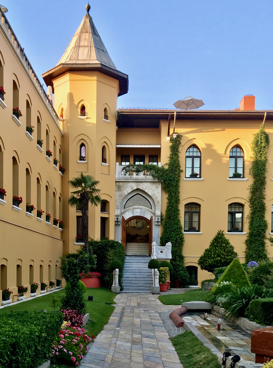 Four Seasons Sultanahmet’s ochre courtyard facade, pointed arched entrance, corner tower and garden path.