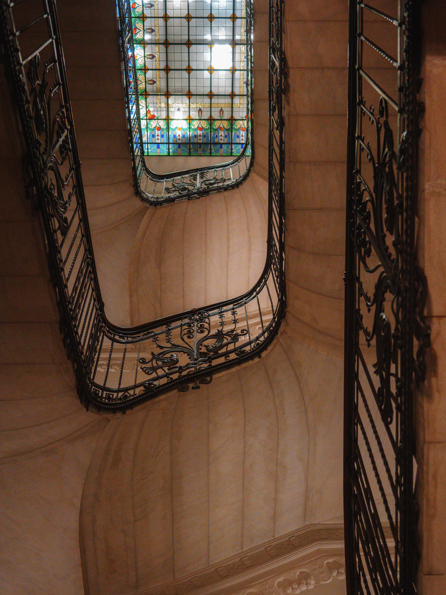 Curving wrought-iron stair rails rise towards a floral stained-glass ceiling at Four Seasons Gresham Palace.