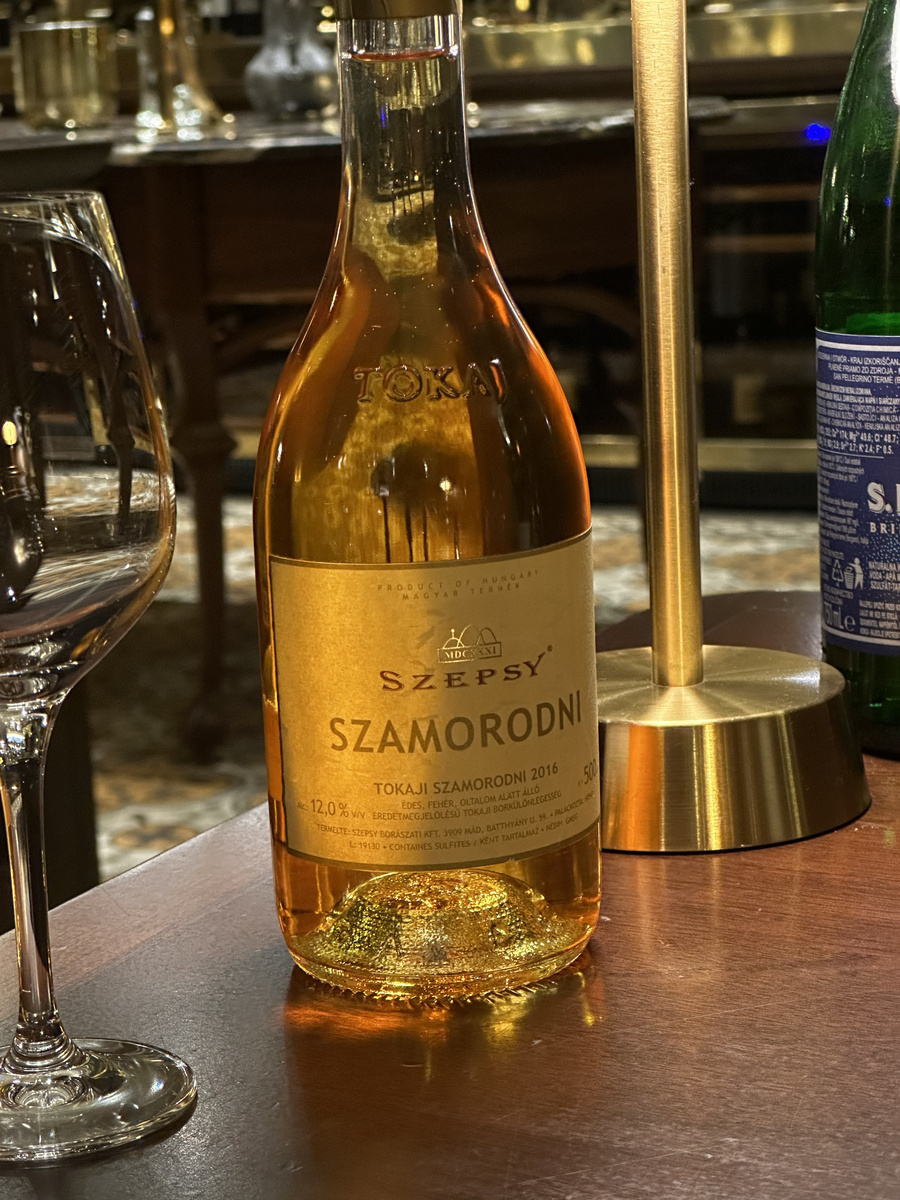 A bottle of Szepsy Tokaji Szamorodni stands beside a wine glass on a hotel table.