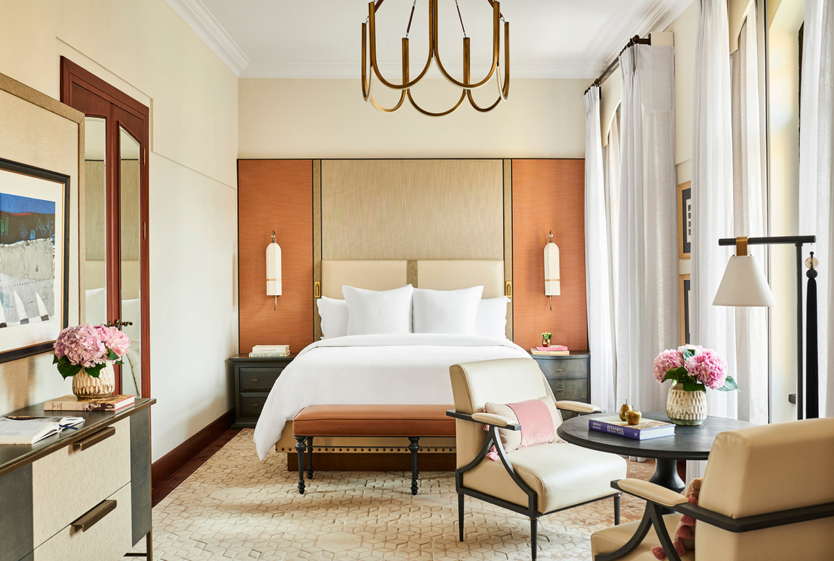 A current Four Seasons Sultanahmet guest room with a pale upholstered bed, warm timber headboard, brass lighting and cream armchairs.