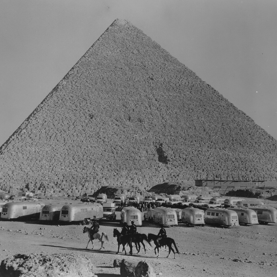 Rows of Airstream trailers camped beneath the Great Pyramid of Giza as riders on horseback cross the foreground.
