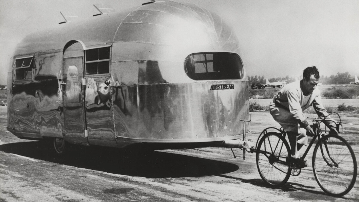 French cyclist Alfred Letourneur pedals a bicycle while towing a polished Airstream trailer in 1947.