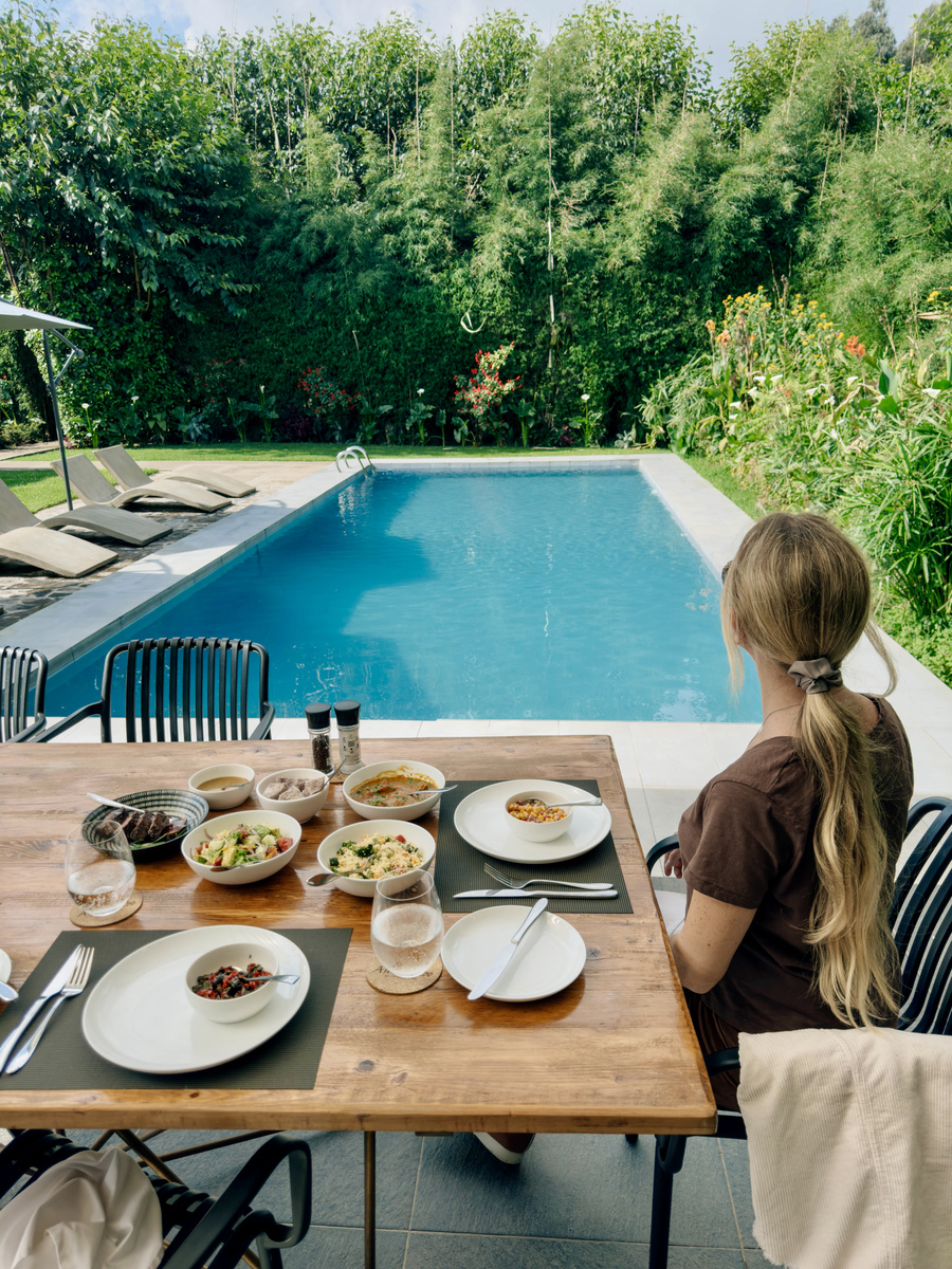 Olga sits at a breakfast table beside Amarembo’s rectangular swimming pool and bamboo garden.